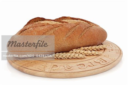 Rye bread loaf on a wooden board with wheat sprigs, over white background.