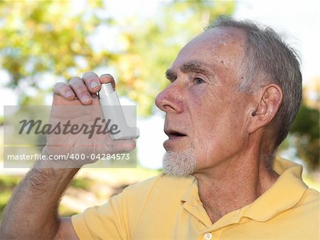 Old man using asthma inhaler out of doors to control allergies. Isolated on white.