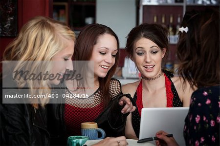 Four cute college girls with a laptop having fun in a cafe over a coffee