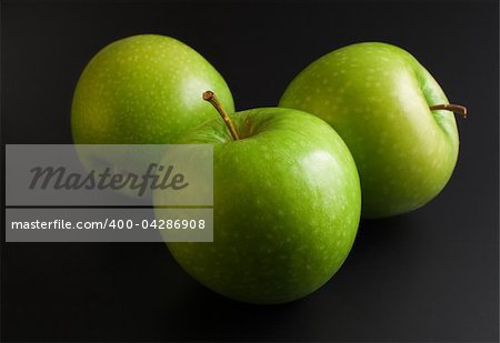 Three fresh ripe green apples close up arranged on dark background