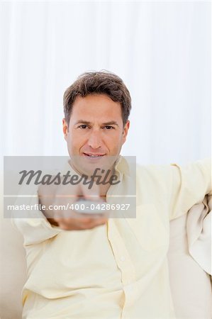 Relaxed man pointing a remote to the camera while relaxing on the sofa