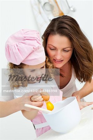 Mother and daughter breaking eggs while cooking together in the kitchen