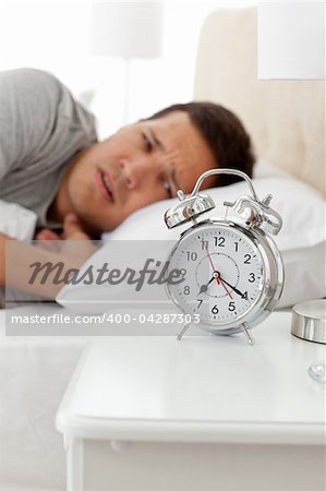 Unhappy man looking at his alarm clock while lying on his bed at home