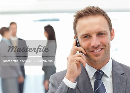 Happy businessman on the phone while his team working on the background