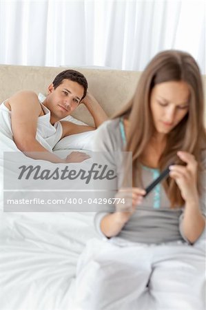 Adorable man looking at his girlfriend filing her finger nails on the bed at home
