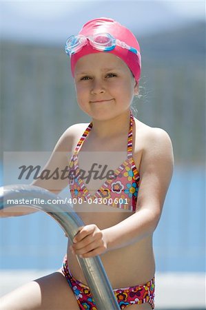 Close-up portrait of smiling cute little child in bathing cap, glasses near swimming pool stairs