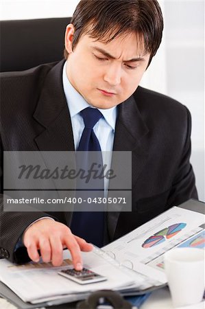 Serious modern business man sitting at office desk and working  with financial documents