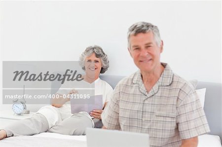 Man working on his laptop while his wife is reading at home