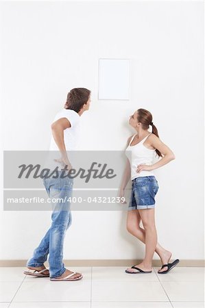Young couple looking at hanging on the wall frame
