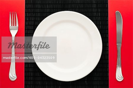 empty white plate on black table with knife and fork on red napkin by the sides of the plate