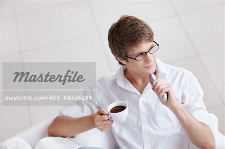 A young man with a cup of coffee and a remote control in hand