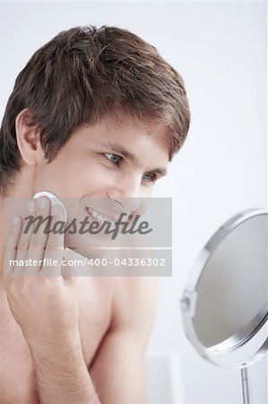 Attractive man rubs the lotion face in the mirror