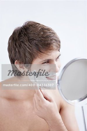 Young man shaving at the mirror on a white background
