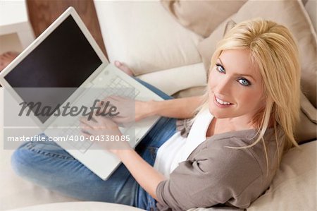 Overhead photograph of beautiful young woman at home sitting on sofa or settee using her laptop computer and smiling