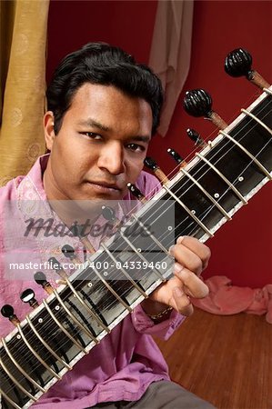 Handsome Indian man in traditional attire plays a Sitar