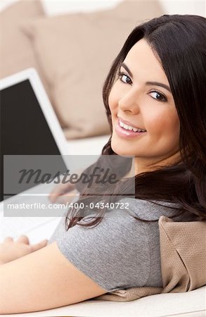 Beautiful happy young Latina Hispanic woman smiling and using a laptop computer at home on her sofa