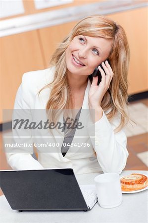 Delighted businesswoman with laptop, coffee and food talking on phone in her office