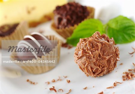 Chocolate truffles with mint leaf, fine chocolate shavings and a yellow cake in the background (Very Shallow Depth of Field, Focus on the front of the first praline)