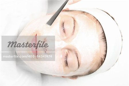 A picture of a young relaxed woman with a facial mask on over white background