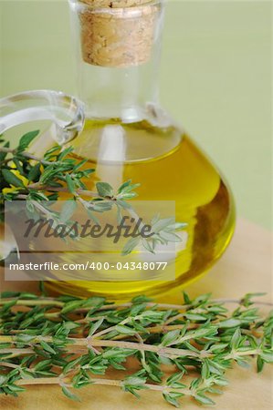 Fresh thyme sprig with olive oil in glassbottle on wooden board and green table mat (Selective Focus)