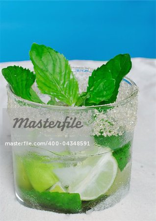 The Cocktail Mojito with Ice Cubes, Mint Leaves and Sugar Rim on Sand and with Blue Background