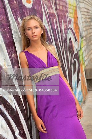 Beautiful teenager in purple dress posing in front of graffiti background