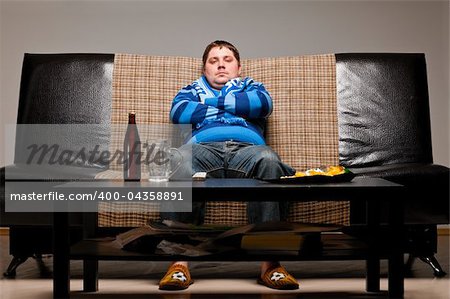 soccer fan is sitting on sofa with beer at home