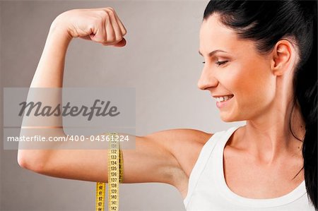 sporty woman is measuring her biceps on grey background