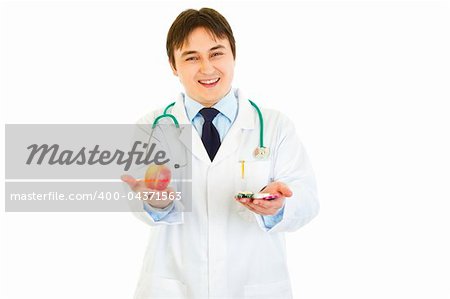Smiling medical doctor with pills in one hand and apple in other isolated on white