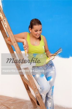 Sexy young woman is looking to the color palette in her hand near the ladder