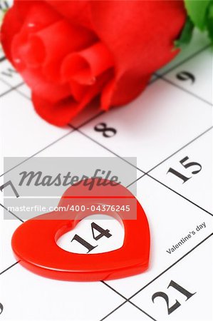 Red heart shape marker and rose on calendar page showing Febraury 14 Valentine's day