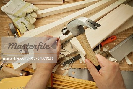Wooden workshop table with tools. Man's arms hammering a nail