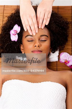 Beautiful happy peaceful sleeping woman at day spa, laying on bamboo massage table with head on pillow wearing a towel getting a facial massage.