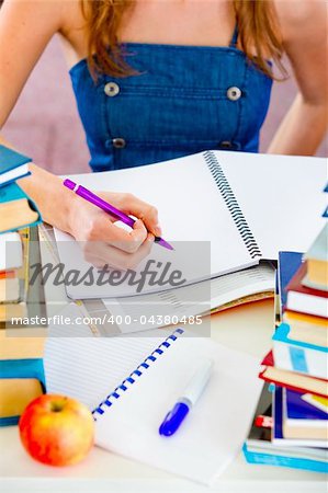 Girl sitting at table with lots of books and doing homework. Close-up