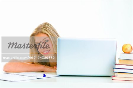 Sitting at table smiling teen girl looking out from laptop
