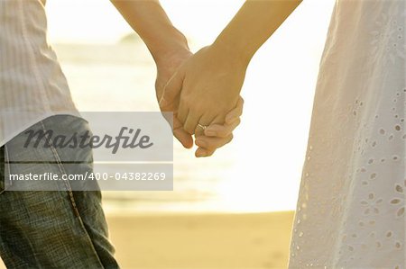 Young adult male and female holding hands on beach at sunset.
