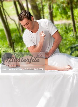 A male masseur giving a massage to a woman outdoors