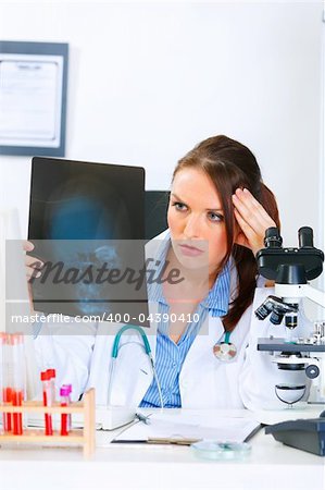 Concentrated medical doctor woman sitting at office table and analyzing patients roentgen