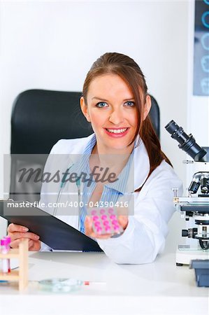 Smiling medical doctor woman sitting at office table and giving prescription drugs