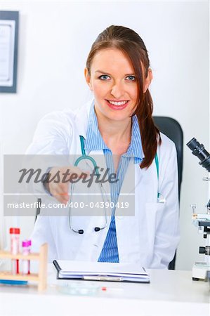 Smiling medical doctor woman stretches out hand for handshake in office