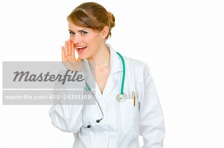 Smiling medical doctor woman holding her hand near mouth and secretly reporting good news isolated on white