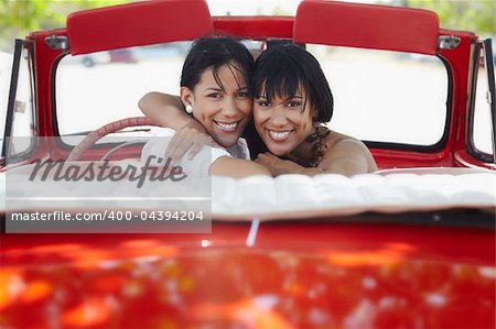 young adult brunette twin women driving convertible red car and looking over shoulders. Horizontal shape, rear view, copy space