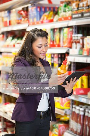 A happy woman using a tablet computer in a supermarket to check out a product