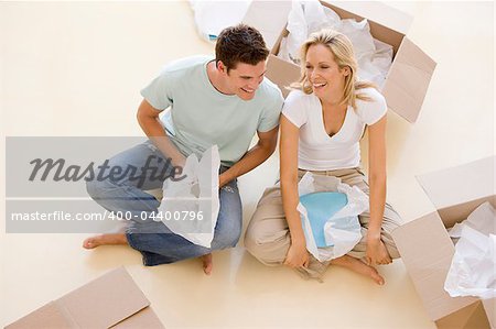 Couple sitting on floor by open boxes in new home smiling