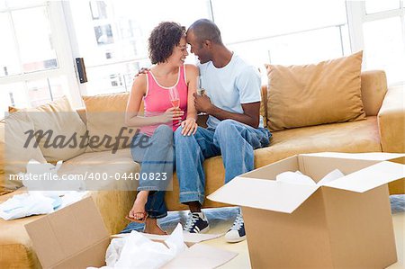 Couple relaxing with champagne by boxes in new home smiling