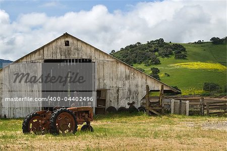 Old wooden barn with rusted tractor sitting out front.