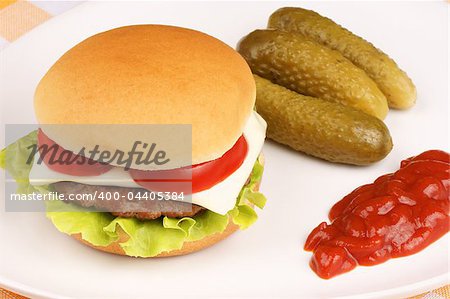 Mini cheese burger with tomato and lettuce and some pickles and ketchup on a white dish.