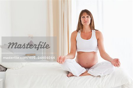 Good looking pregnant female doing yoga on a bed in her apartment