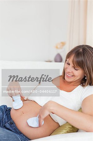 Pregnant woman playing with baby shoes while lying in her living room