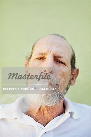 portrait of mature white man looking at camera against green wall with cigarette in mouth. Copy space
